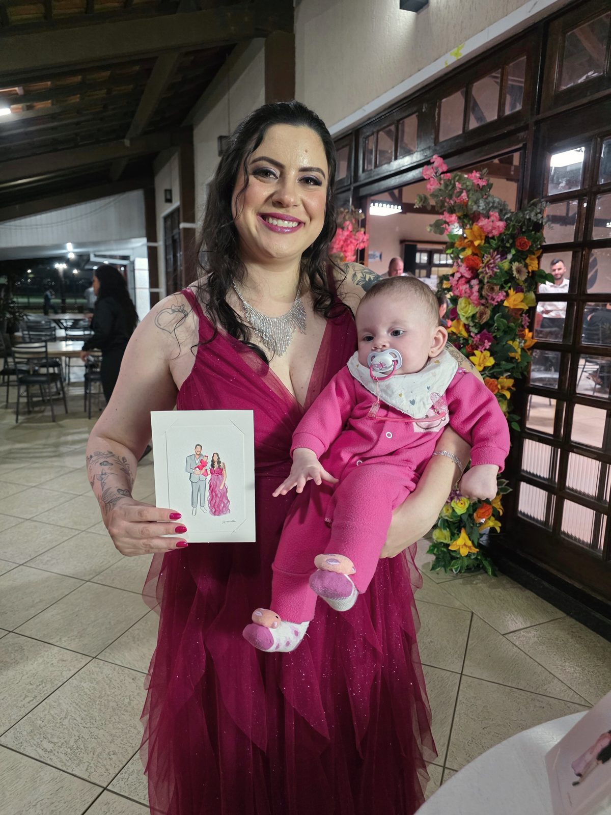 Mãe com a bebê no colo segurando o retrato das duas