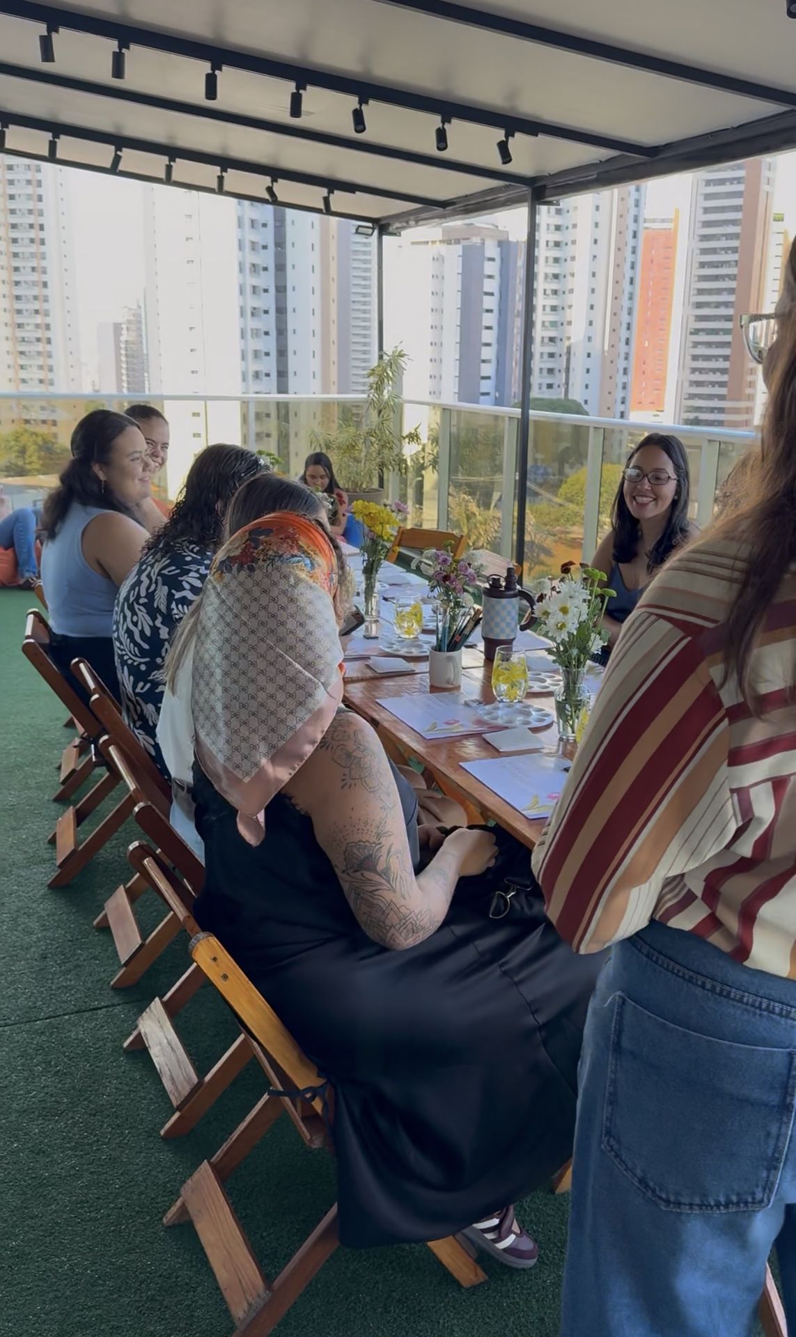 A turma reunida na mesa comprida da varanda, pintando junta